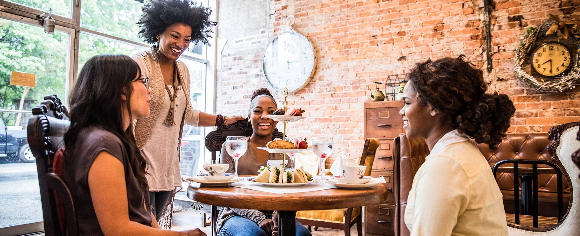 Four women sit and stand around a small round dining table with a tiered food tray at a restaurant in Atlanta, Georgia.