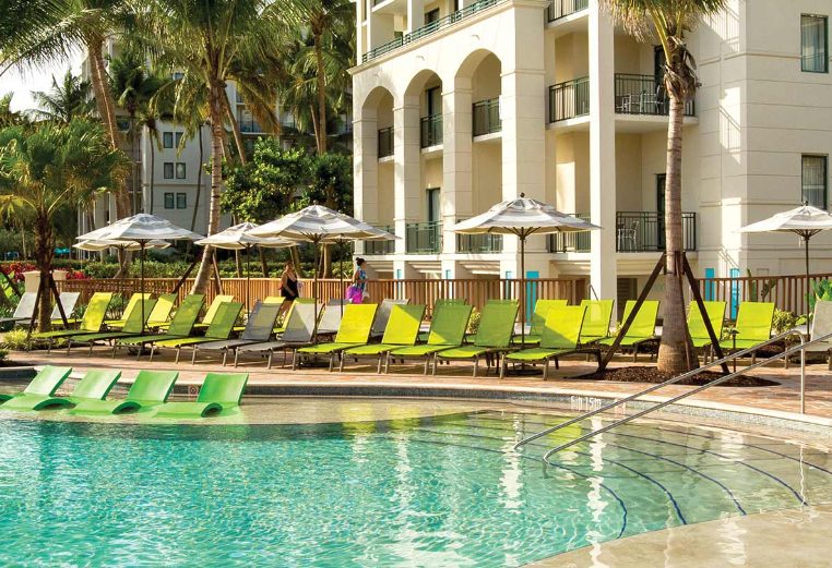 Bright green pool chairs and palm trees surround the shimmering pool at a Margaritaville Vacation Club resort.