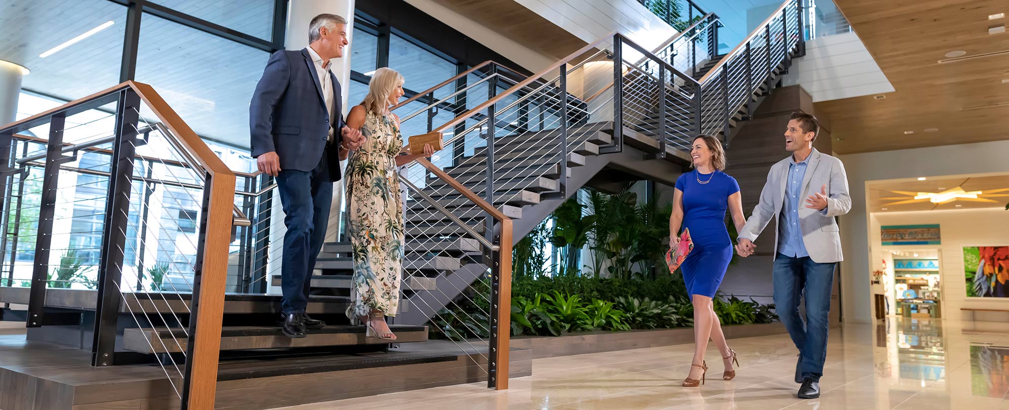 Two couples, each holding hands, greet each other at the bottom of a staircase at a Margaritaville Vacation Club resort.