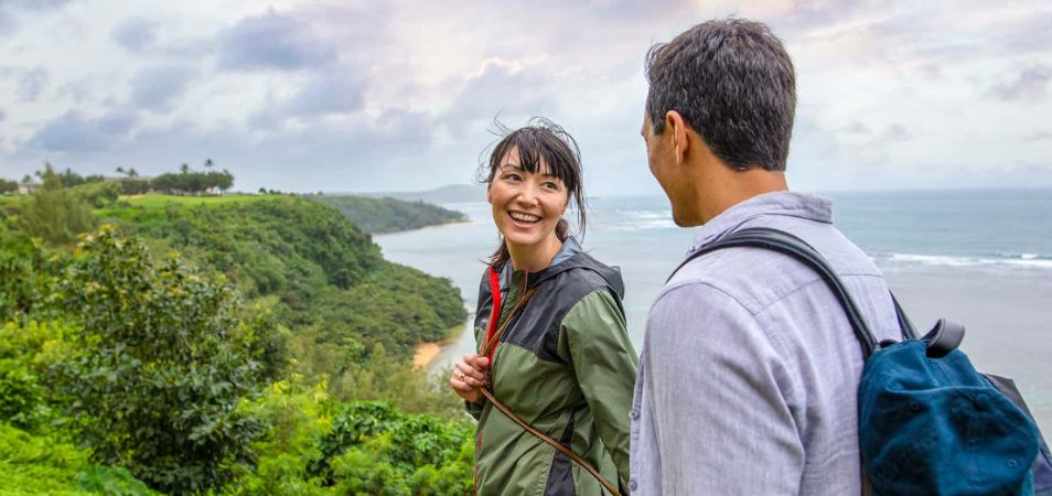 A couple on vacation hiking through lush mountains overlooking the ocean. 