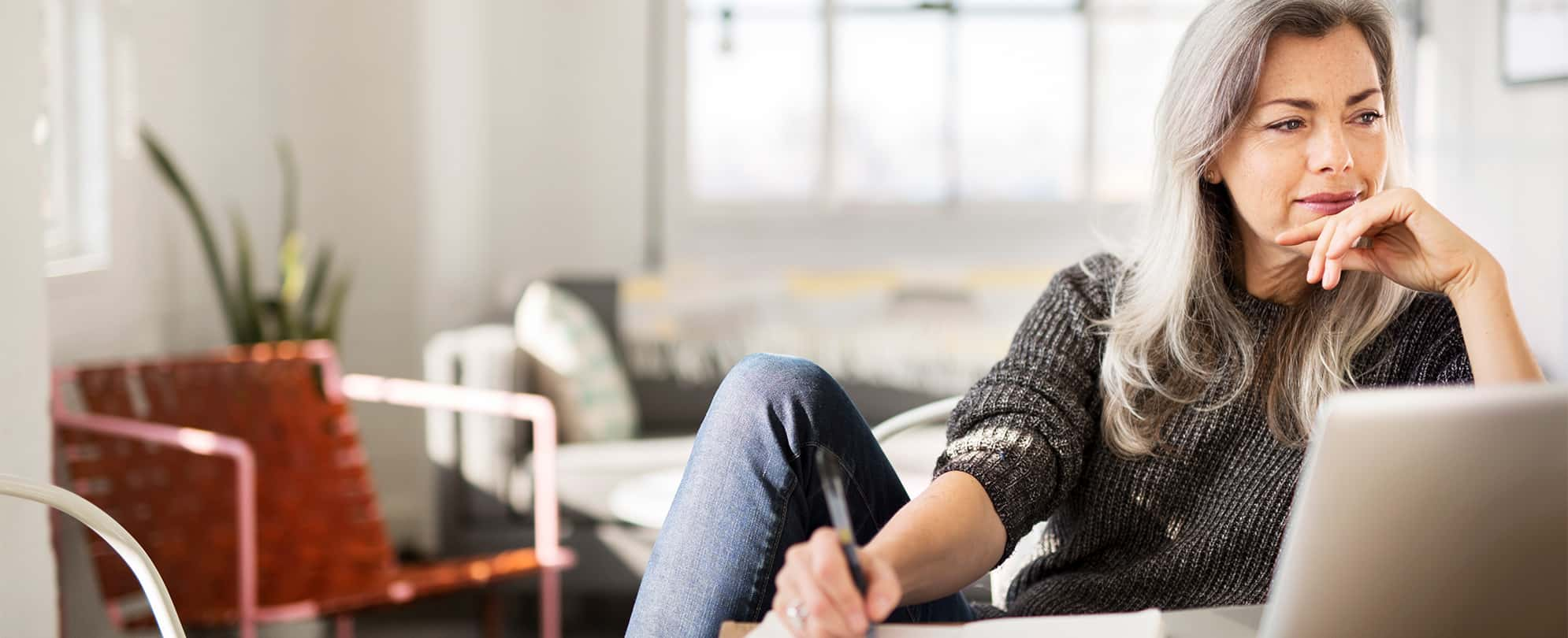 A woman sitting comfortably in a chair holding a pen writing. 