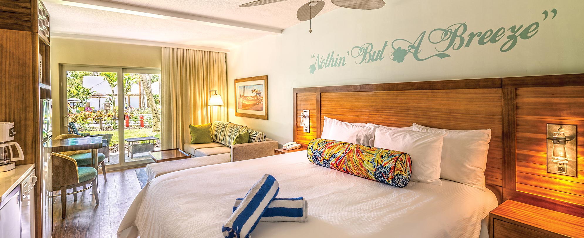 "Nothin' But A Breeze" written on the wall above a resort bed with a wood headboard in a Margaritaville Vacation Club suite.