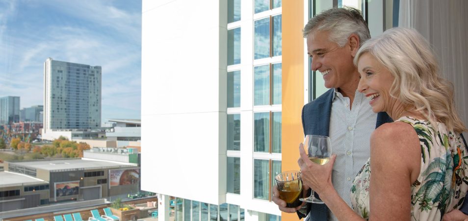 Couple holding drinks stand out on the balcony of their Presidential Reserve suite at a Margaritaville Vacation Club resort.