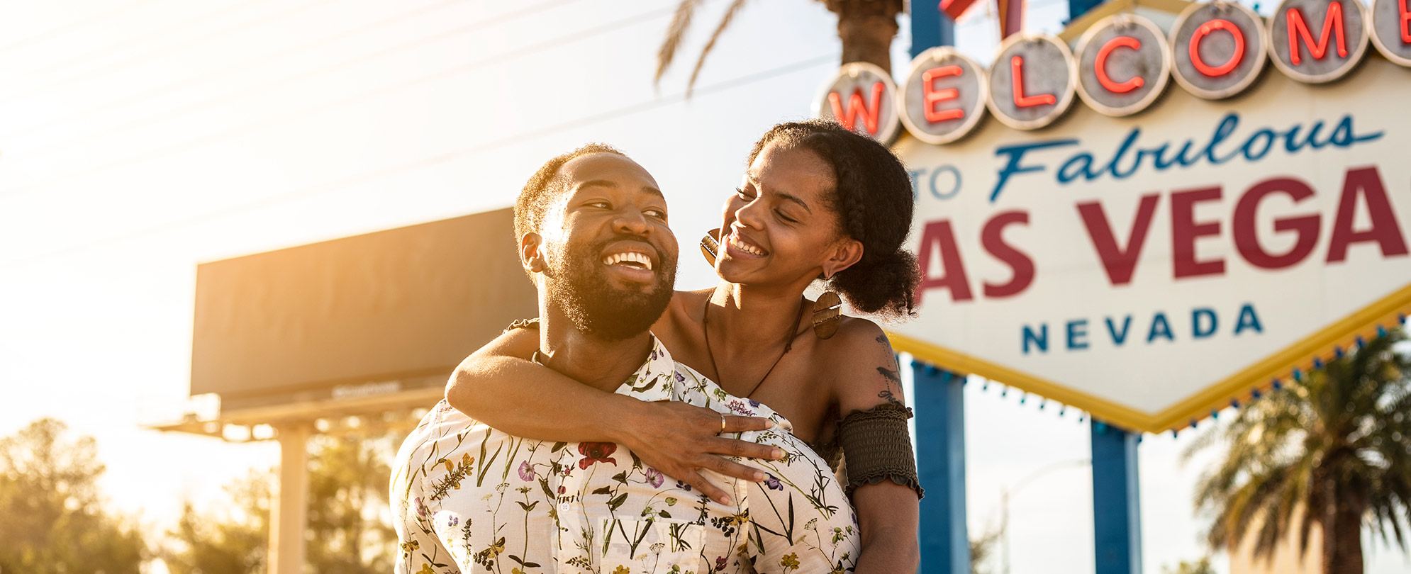 A man gives a woman a piggy back ride in front of Las Vegas sign that reads "Welcome To Fabulous Las Vegas, Nevada."