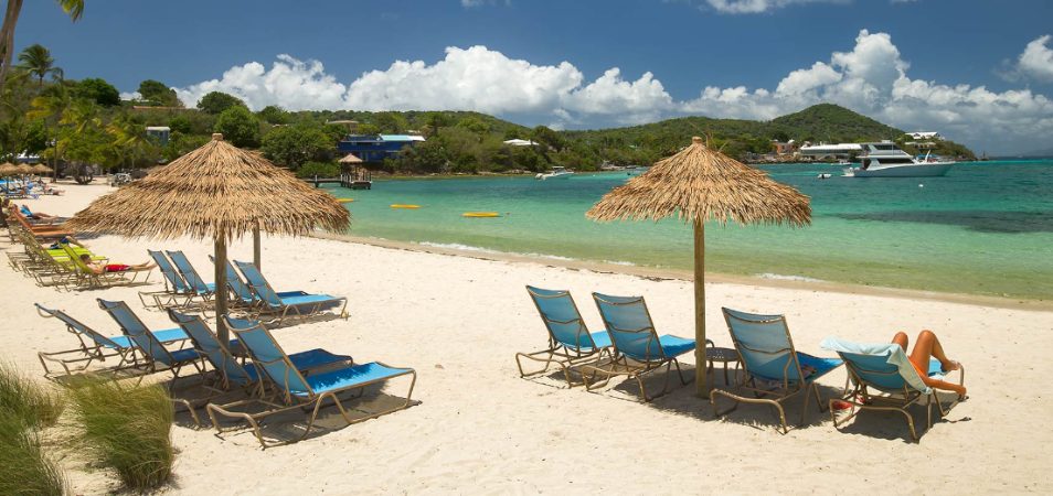 Guests lay by the ocean on beach chairs under straw umbrellas at Margaritaville Vacation Club by Wyndham - St. Thomas.