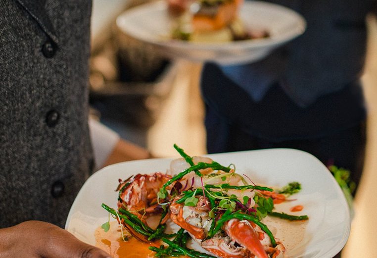 Close-up shot of a waiter holding a plate of seafood and vegetables, about to bring it to a table.